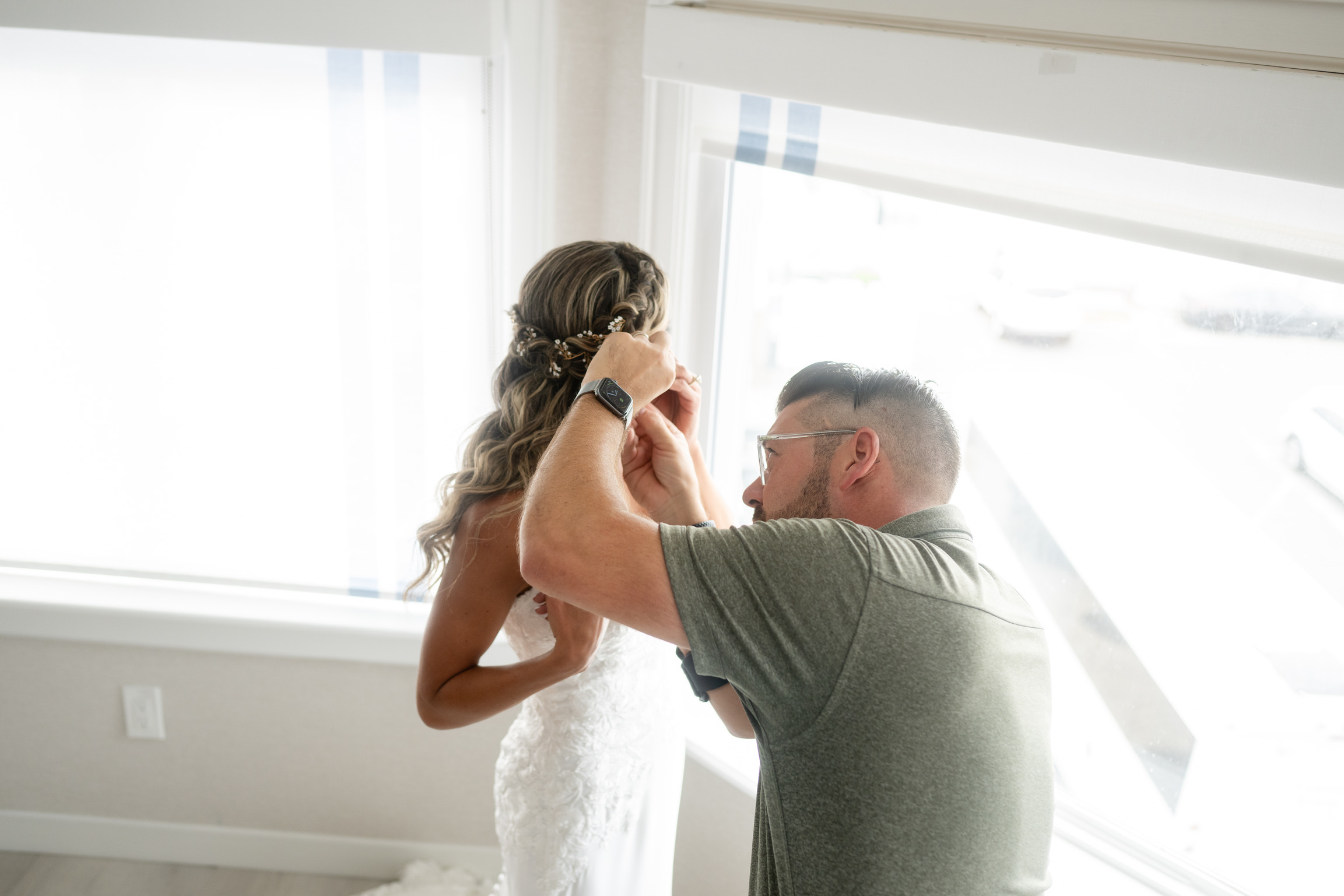 John carefully arranging a bride's hairpiece in soft window light.